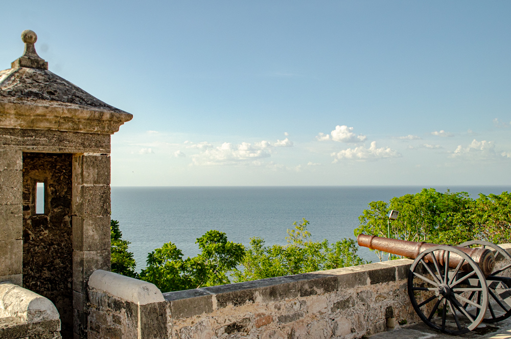  A view of the ocean from a stone fort in Campeche, with a historical cannon and a guard tower