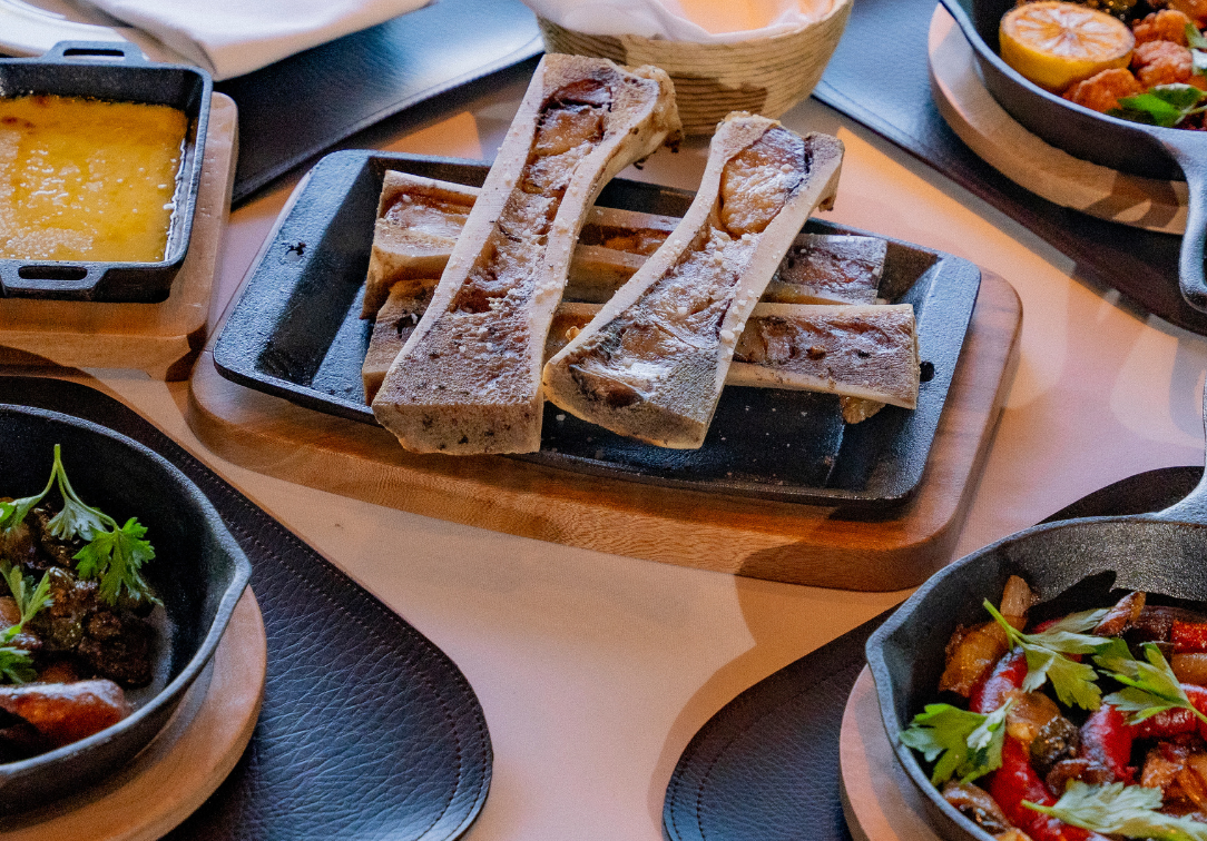 Close-up of roasted bone marrow served on a cast iron platter, surrounded by other small-plate appetizers in cast iron skillets, indicating a high-end corporate dining experience. The meal features gourmet Argentine cuisine ideal for MICE industry events, executive dinners, incentive group catering, or a premium networking reception with exquisite food