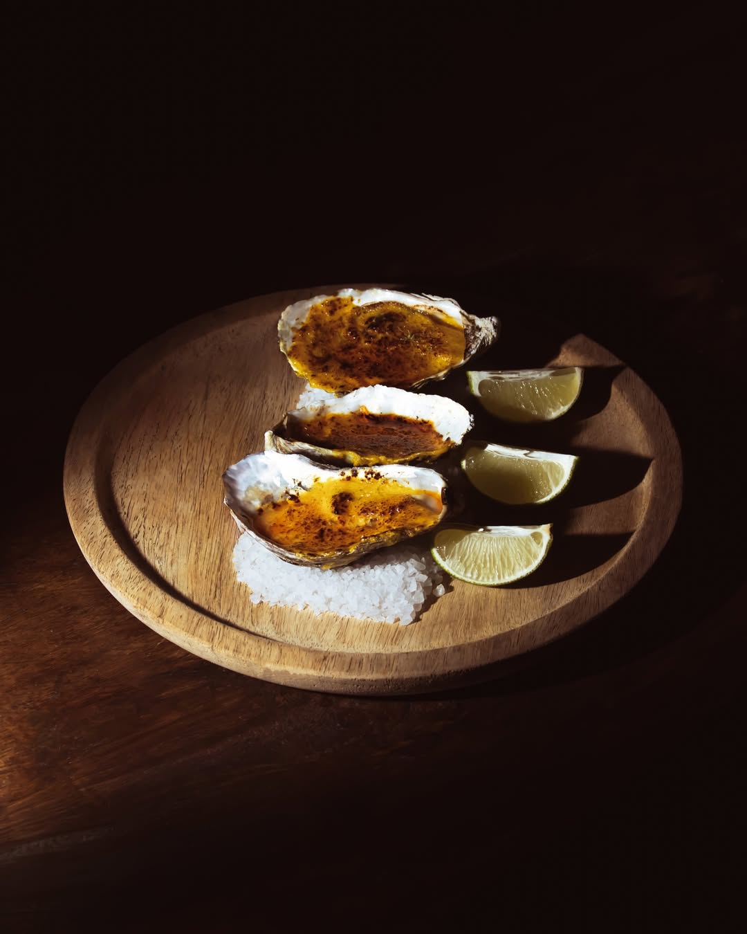 Close-up of gourmet grilled oysters served on a wooden plate with lime wedges, presented in a fine-dining setting, ideal for corporate dinners, incentive travel programs, and high-end group dining experiences.