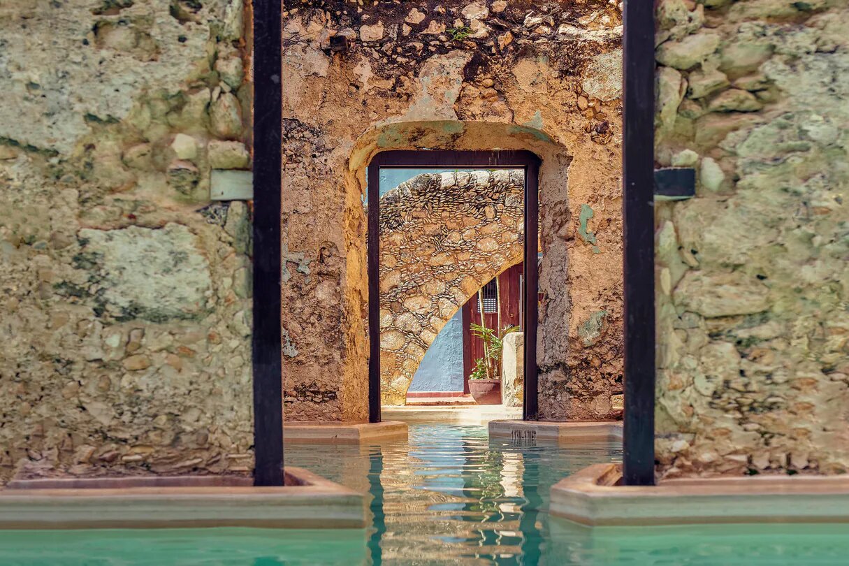 Luxury MICE event venue in Campeche, Mexico: Dramatic view of the striking blue waters of the swimming pool area at Hacienda Puerta Campeche, an ideal space for unique cocktail receptions, intimate corporate retreats, and incentive group welcome parties. The restored 17th-century colonial architecture, with exposed beams and tiled floors, offers an exclusive backdrop for high-end meetings and events.