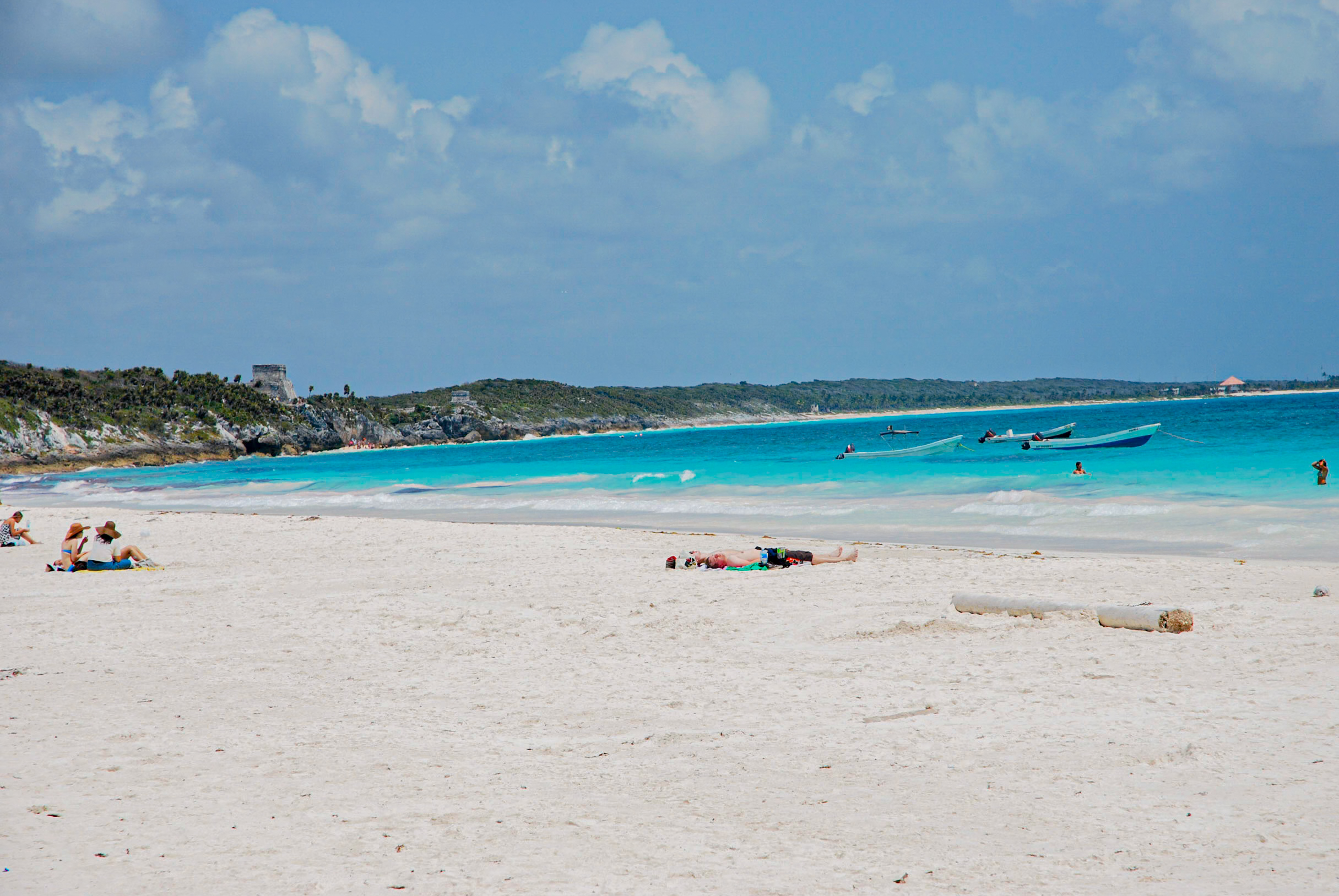 Idyllic Tulum beach scene in Mexico featuring crystal-clear turquoise waves, white sand dunes, ancient Mayan ruins perched on cliffs, scattered lounge chairs, and distant boats, offering an inspiring backdrop for MICE conferences, executive incentive trips, and outdoor team-building workshops in a historic tropical paradise.