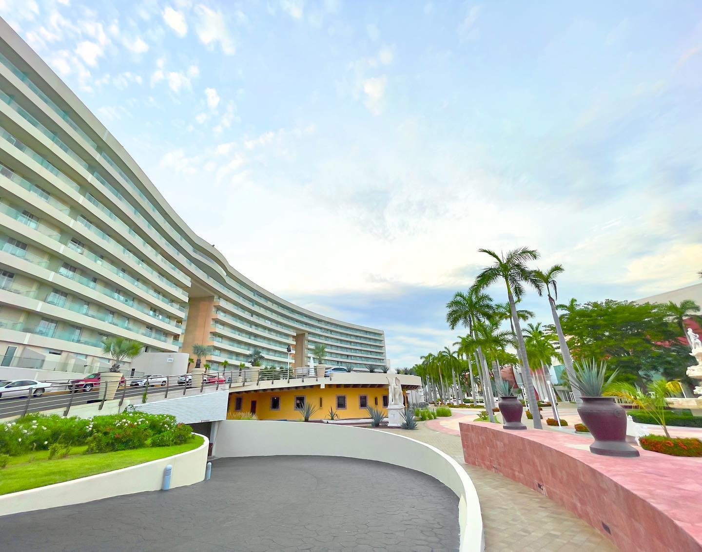 Exterior view of a modern curved luxury hotel in Acapulco, Mexico, featuring palm trees, tropical landscaping, and a sweeping driveway entrance, ideal as a MICE venue for meetings, incentives, conferences, exhibitions, and incentive travel programs in a premier Mexican destination.