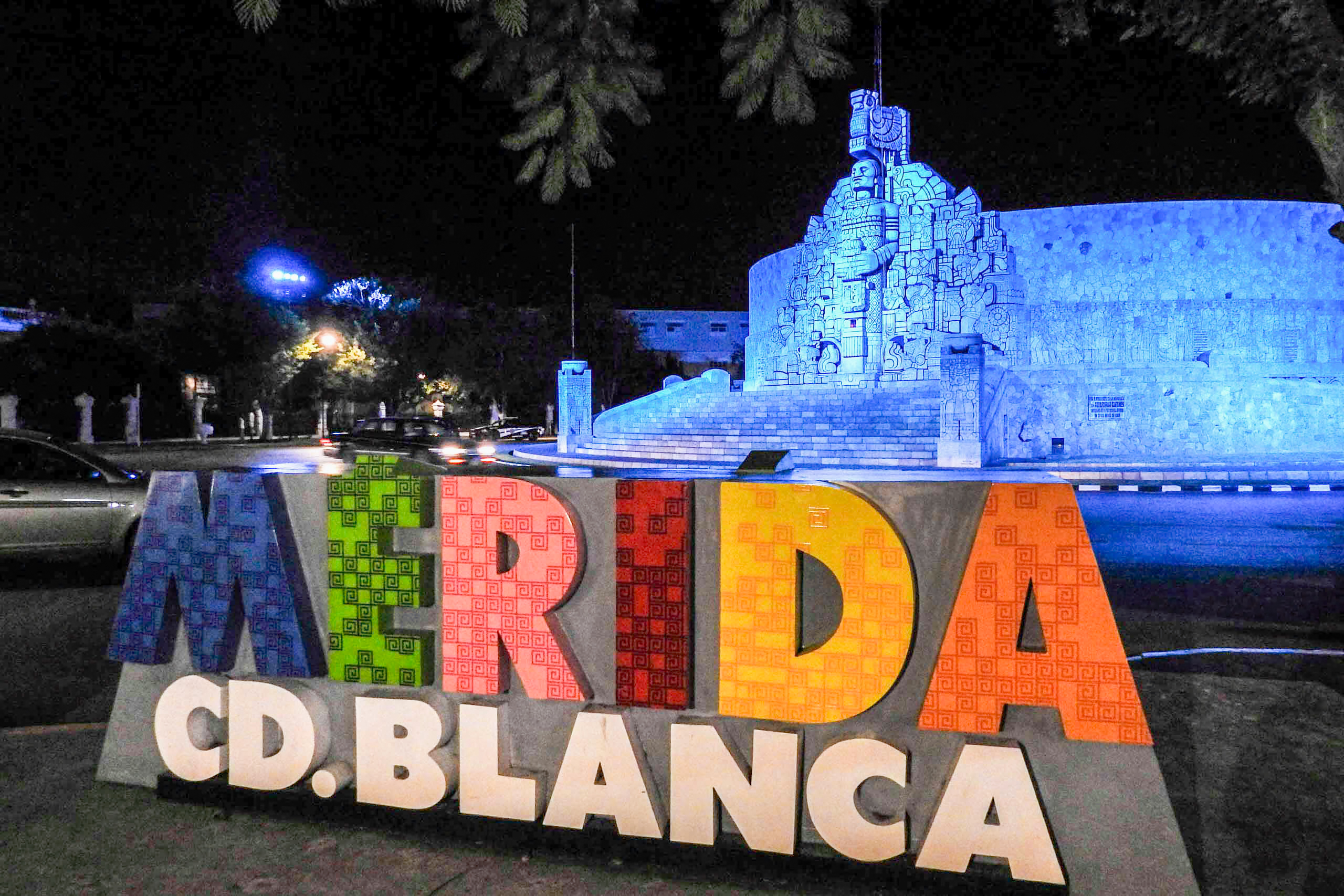 The colorful "Mérida Cd. Blanca" sign in front of the illuminated Monumento a la Patria at night. This monument is a key city landmark and a popular gathering point, creating a vibrant atmosphere for evening excursions for MICE attendees.