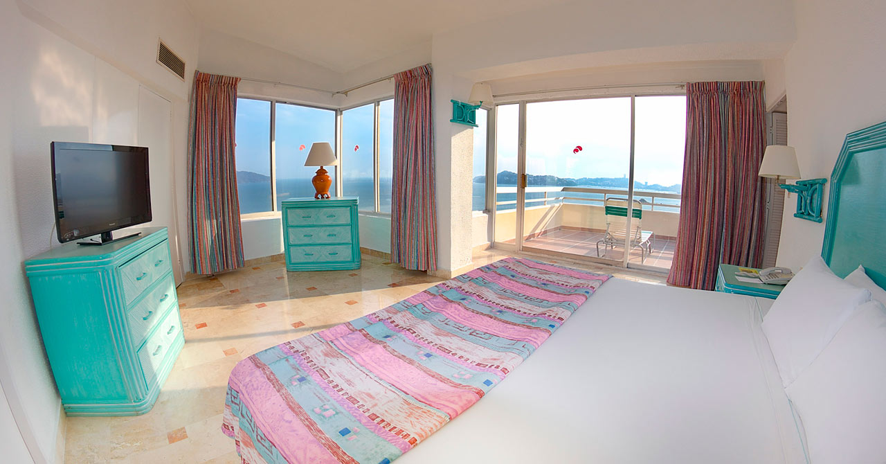 A bright, spacious penthouse room at the Playa Suites Hotel in Acapulco, featuring a king-sized bed, marble-like floors, and turquoise and pink tropical decor. The room boasts panoramic windows and a sliding door leading to a balcony with ocean views. This penthouse is an ideal accommodation for VIP MICE delegates or a rewarding choice for incentive travel winners, offering a premium experience and great views for high-level corporate guests.