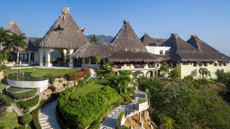 A view of the distinctive, pyramid-shaped high-rise hotel in Acapulco from the main entrance road, lined with lush landscaping and tall palm trees under a bright sky. The road leads toward the large structure, which symbolizes a high-capacity MICE venue perfect for welcoming hundreds of conference attendees and large incentive groups to a major tropical resort destination.