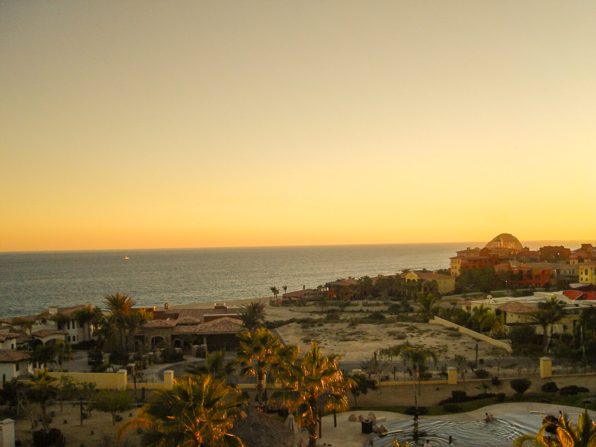 A panoramic view of the Los Cabos coastline, with luxury villas and resorts nestled along the shore at sunset. The peaceful seaside setting is perfect for rewarding incentive travel experiences and relaxed MICE events.