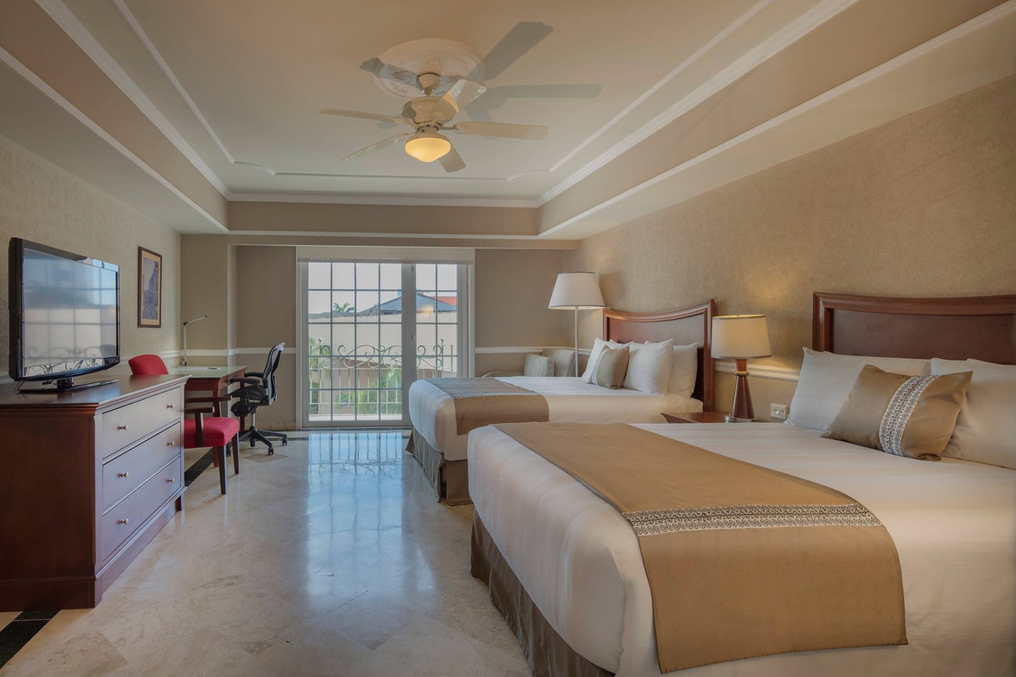 Convention accommodations for MICE delegates at Presidente InterContinental Mérida: Interior view of a spacious hotel room featuring two double beds, marble floors, a ceiling fan, a dedicated work desk, and a television, ideal for accommodating conference and convention attendees.