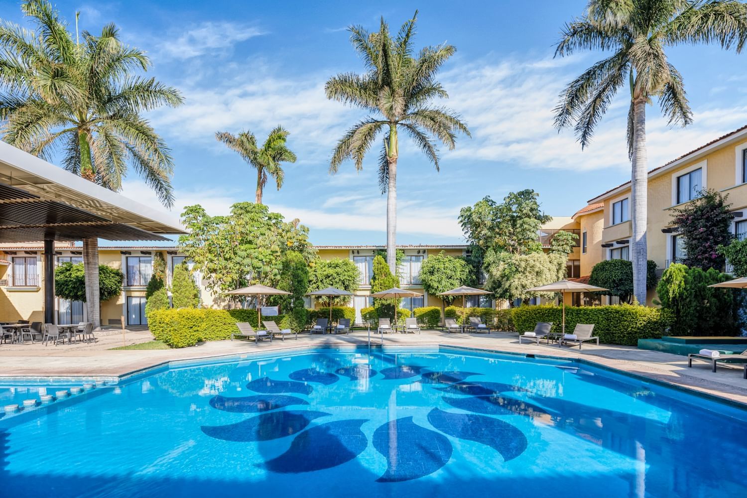Resort-style outdoor pool with tropical landscaping and lounge seating, ideal for MICE incentive travel and group relaxation in Oaxaca, Mexico.