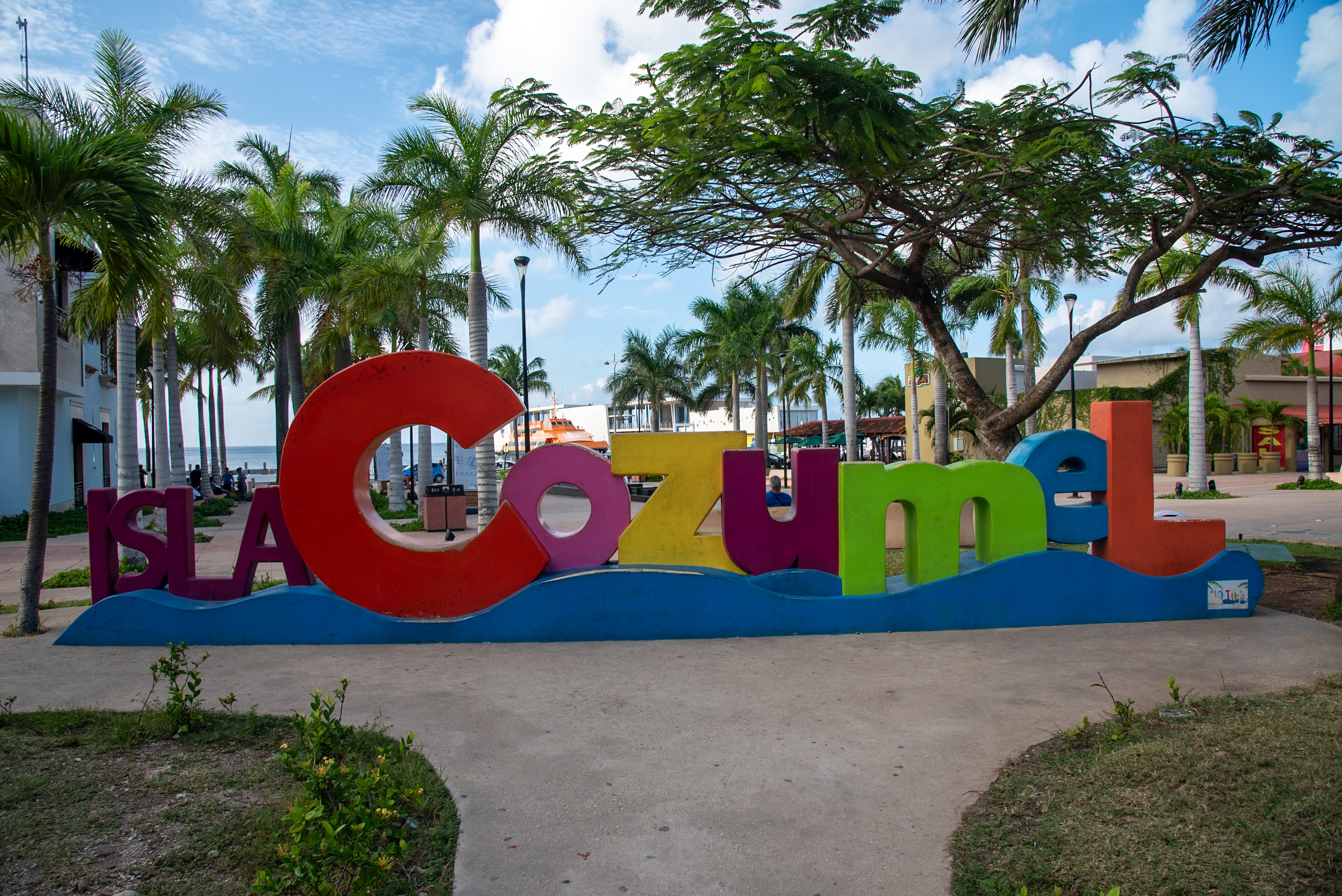 Colorful 'Isla Cozumel' welcome sign in San Miguel, Cozumel, set against a vibrant blue sky with palm trees, representing an ideal, accessible MICE destination for corporate events, incentive travel, conferences, and group meetings in Mexico's Caribbean