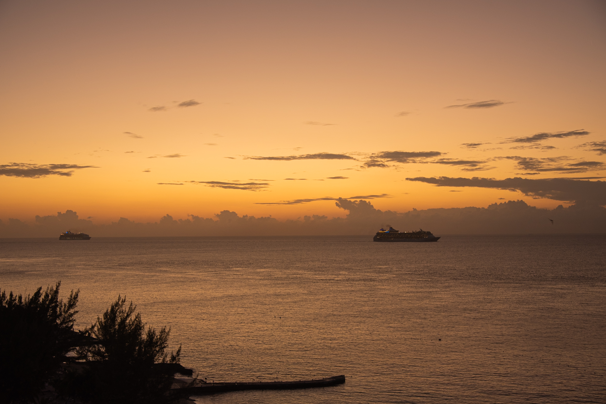 A breathtaking panoramic view of the golden sunset over the tranquil ocean, featuring two prominent cruise ships on the horizon and a pier in the foreground. Ideal for MICE industry event promotions, showcasing luxurious incentive travel, corporate retreats, and conference venue possibilities at sea or along coastal destinations. Emphasizes serene settings, unique experiences, and stunning backdrops for meetings, incentives, conferences, and exhibitions